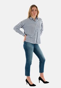 Camisa de botones a rayas en azul claro y blanco, combinada con jeans ajustados azules y tacones altos negros. La camisa tiene un collar clásico y mangas largas.