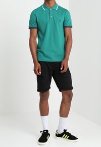 Tyrkysové polo tričko s bílým límečkem a manžetami, černé kraťasy s roztrhnutými detaily, černé a zelené tenisky, bílé ponožky.