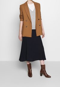 Brun dubbelknäppt kavaj över en grå cardigan, tillsammans med en plisserad svart kjol och bruna ankelboots i krokodilstruktur.