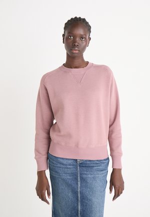 Rosa Sweatshirt mit Rundhalsausschnitt, gerippten Bündchen und Saum. Kombiniert mit einem Jeansrock. Der Stoff scheint weich mit einer glatten Textur zu sein.