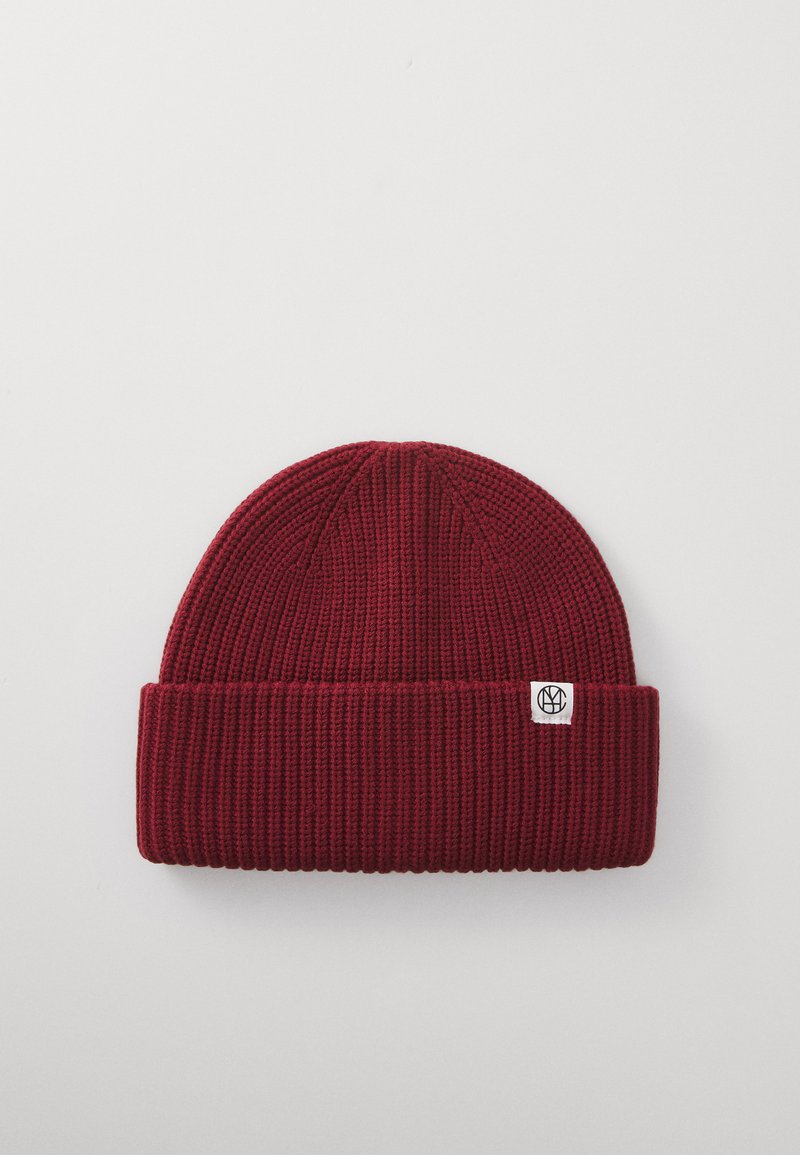 Mørkerød ribstrikket beanie med foldet kant og lille hvidt mærke med et sort cirkulært logo, præsenteret på en ensfarvet lys baggrund.