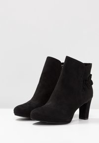 Černé semišové kotníkové boty s kulatou špičkou, středně vysokým blokovým podpatkem a řaseným akcentem po straně. Zip na vnitřní straně.