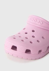 Roosa klots, valmistatud kergest sünteetilisest materjalist, millel on õhutusavad, tekstuuriga pind ja rihmal tõstetud logo.