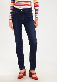 Mörkblå smala jeans i denim, med framfickor och ihopfällbar dragkedja, i kombination med ljusröda patenterade klackskor.