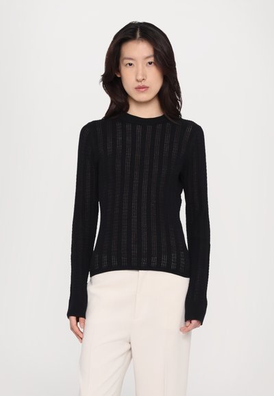 Sort strikket langærmet sweater med vertikale striber og ribbede manchetter og kant. Bæres med lyse bukser.