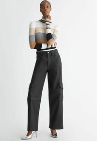 Maglione a collo alto a righe e coste in tonalità neutre, abbinato a pantaloni cargo neri con tasche laterali. Tacchi a punta argentata completano il look.