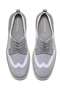 Zapatos de punto grises con acentos blancos, presentan un superior texturizado, cordones grises y una suela de color claro. Marca visible en la plantilla.