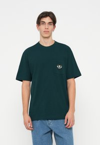Temnozeleni bombažni T-shirt s kratkimi rokavi, okroglim izrezom in sprednjim žepom, ki vsebuje majhen večbarven vezen motiv.