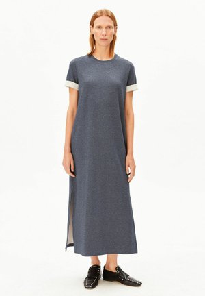 Robe grise mi-genoux avec un col rond et des manches courtes bordées de blanc. Présente des fentes latérales et une coupe décontractée. Portée avec des chaussures noires.