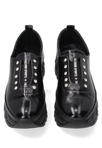 Schwarze, glänzende Slipper mit Nietenakzenten, ausgestattet mit einer dicken, strukturierten Sohle und einer Stoffzunge mit dem Text "FASHION SPORTS".