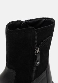 Schwarze Knöchelstiefel aus einer Kombination aus Wildleder und Leder, mit einem silbernen Reißverschluss und strukturierten Akzenten.