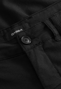 Fekete farmernadrág Gabba márkájú címkével, fekete gombbal és finom varrási részletekkel. Az anyaga sima tapintású és tartós kivitelű.