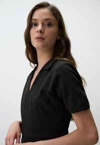 Schwarze Bluse mit Nadelstreifen und Kragen, mit kurzen Ärmeln und V-Ausschnitt. Glatte Textur mit dezenten Musterakzenten.