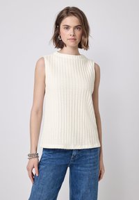 Ærmeløs cremetop med ribbet tekstur, rund halsudskæring og lige kant. Kombinationen med blå jeans skaber et afslappet look.