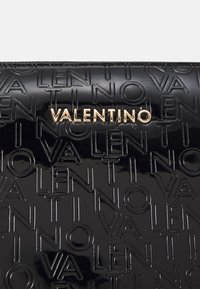 Clutch de couro envernizado preto com padrão em relevo do logotipo 'VALENTINO' e ferragens em tom dourado. Textura suave com um acabamento brilhante.