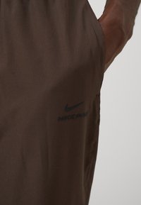 Shorts Nike Pro marron avec une texture lisse, arborant un logo noir sur le côté. Le design met l'accent sur le confort et la performance.