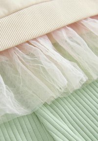 Vaaleanpastellinvärinen, ribattu kangas alaosassa, kerrostettuna pehmeällä, läpinäkyvällä, röyhelöisellä tullellä vaaleanpunaisena ja kermana, jonka päällä on beige ribattu vyö.