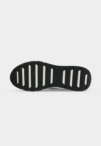 Semelle de chaussure noire avec des rainures horizontales blanches et le logo "BOSS" embossé au centre, présentée sur un fond uni clair.