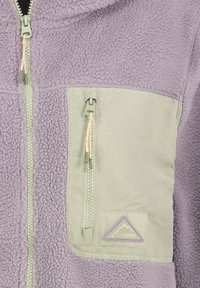 Lavendelfarbene Fleecejacke mit hellgrünem Reißverschluss an der Brusttasche und passenden zentralen Reißverschlüssen, mit einem Outdoor-Logo-Aufnäher.