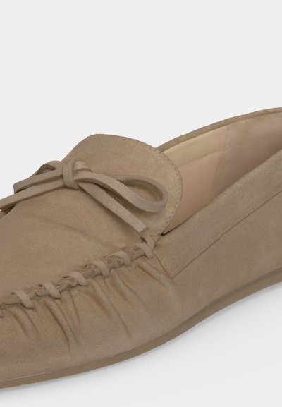 Mocassin en daim beige avec un détail nœud sur le dessus et des coutures froncées le long du bord avant.