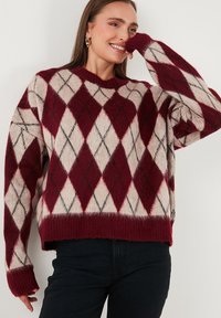 Rood en crèmekleurig argyle-patroon trui met geribde manchetten en zoom. Zachte, gestructureerde breimateriaal. Ontspannen pasvorm met grijze accenten.