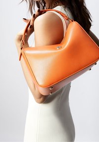 Oranssi nahkakäsilaukku, jossa on kaareva muotoilu, jossa on kultasäväyksen yksityiskohta ja vaaleampaa oranssia pohjaa.