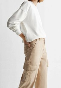 Bílá bavlněná mikina s dlouhými rukávy a žebrovanými manžetami, zkombinovaná s béžovými cargo kalhotami s bočními kapsami a volným střihem.