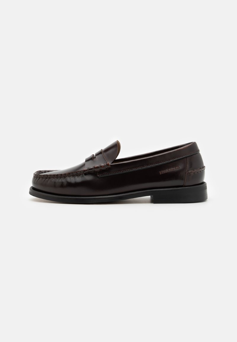Brown leather loafers with a rounded toe, detailed stitching, and a flat rubber sole. Minimalist design with a low heel and subtle branding.