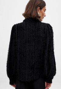 Black textured blouse featuring vertical stripes with frayed edges, long sleeves, a high collar, and buttoned cuffs.