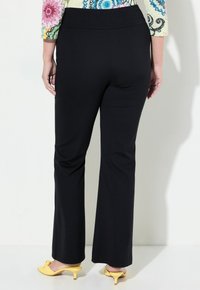 Pantalons noirs évasés avec une taille élastique, tissu lisse et silhouette ajustée. Associés à des chaussures à talons kitten jaunes.