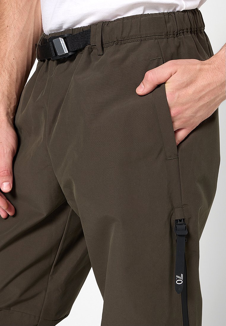 Pantaloni cargo in verde oliva, con vita elastica e cintura, tasche laterali e dettagli con tasca con zip. Il tessuto sembra liscio e leggero.