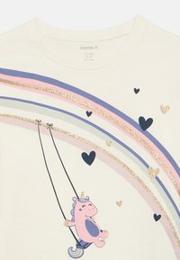 Różowo-fioletowy jednorożec ze złotymi brokatowymi detalami, huśtający się na tęczy z złotymi i granatowymi sercami na kremowej tkaninie.