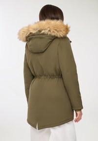 Oliwkowa parka z kapturem wykończonym sztucznym futrem, z dopasowaną talią i bocznymi rozporkami na dole, charakteryzująca się gładkim, matowym wykończeniem.