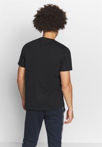 Sort kortærmet t-shirt set bagfra, med en klassisk pasform og glat struktur. Blandt andet med navy bukser med sidelogo-detaljer.