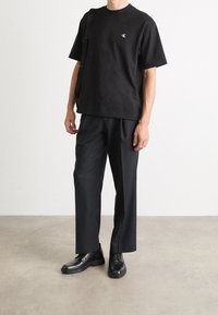 Czarna bawełniana koszulka z małym białym logo, zestawiona z luźnymi czarnymi spodniami i czarnymi butami. Prosty fason i swobodny krój.