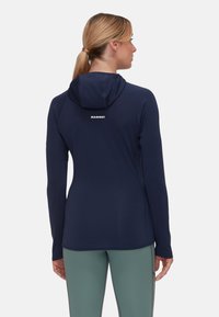 Granatowa bluza z długim rękawem z teksturowanej tkaniny, o dopasowanym kroju i kangurzej kieszeni. Logo "MAMMUT" w białym kolorze na górnej części pleców.