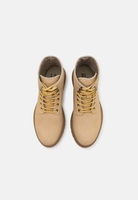 Bottines en cuir tan avec bouts ronds, accents beiges et lacets jaunes. L'intérieur est doublé et dispose d'une semelle intérieure rembourrée.