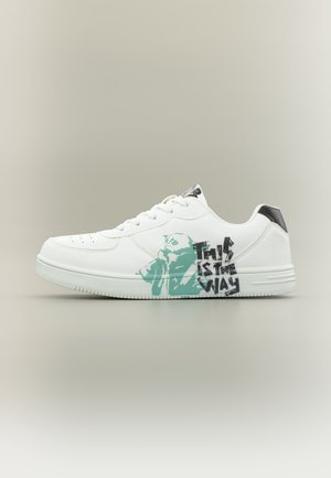 Baskets blanches avec un motif vert représentant un personnage et un texte noir indiquant "This is the way" sur le côté, avec un détail noir sur la languette du talon.