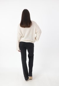 Maglione in crema chunky con una vestibilità rilassata e texture a coste, abbinato a jeans neri skinny e tacchi beige.