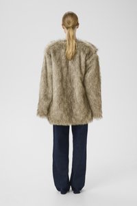 Mākslīgā kažokāda gaiši brūnā krāsā ar mīkstu tekstūru un plašu griezumu, kombinēta ar tumši zilām brīvām džinsu biksēm.