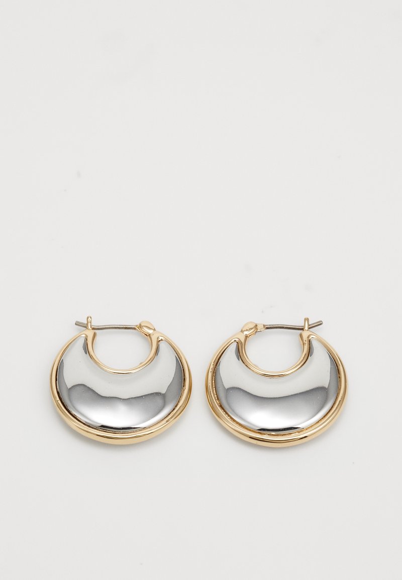 Paire de boucles d’oreilles en forme de croissant avec centres lisses couleur argent et bords dorés sur un fond clair.