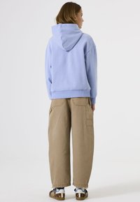 Sudadera azul claro de corte relajado con capucha, combinada con pantalones cargo holgados en color beige con bolsillos laterales, y zapatillas con estampado.