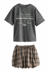 Grå grafisk T-shirt med korte ærmer, der har hvid tekst; parret med en sort og tan ternet kort nederdel med elastisk talje.