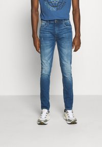 Farkut sinisestä denim kankaasta, joissa on hieman haalistunut viimeistely, etutaskut ja klassinen viiden taskun muotoilu. Yhdistetty valkoisiin nilkkureihin.