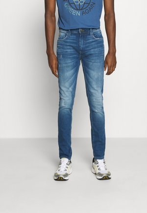 Fitted blå denimjeans med en lätt blekt finish, utrustad med framfickor och en klassisk femficksdesign. I kombination med vita sneakers.