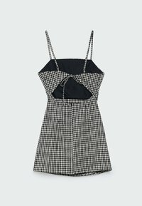 Sort og hvid ternet kjole med tynde stropper, udskæringsdetalje og bånd i taljen. Flared skørt design med en tætsiddende overdel.