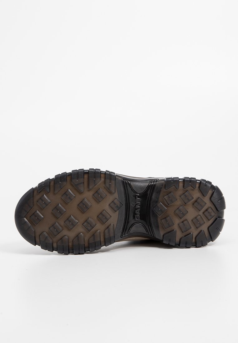 Semelle extérieure en caoutchouc noir avec un motif de grip texturé, présentant des studs hexagonaux surélevés et une semelle intermédiaire de couleur claire contrastante.