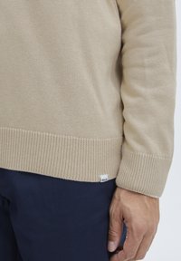 Beige Strickpullover mit geripptem Saum und Bündchen, aus strukturiertem Stoff gefertigt. Klein etikett mit "ISOLID" ist unten links sichtbar.