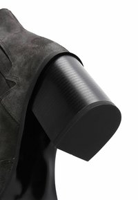 Black suede ankle boot featuring a cylindrical, textured black heel and a smooth, shiny sole, highlighting modern design contrasts.