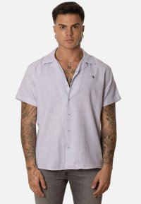 Camisa de manga corta, abotonada, en un suave color lavanda, de tejido texturizado, con cuello y pequeño detalle de logo en el lado izquierdo del pecho.